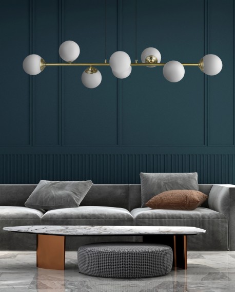 Lampa Fino W8 z sześcioma białymi kulami w szczotkowanym złocie, zawieszona w przestronnej jadalni z ciemnozieloną ścianą i sofą