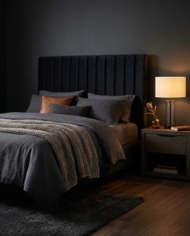 Elegancka lampa nocna Leona Lumina Deco na szafce nocnej w sypialni z ciemnym łóżkiem