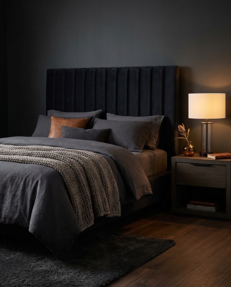 Elegancka lampa nocna Leona Lumina Deco na szafce nocnej w sypialni z ciemnym łóżkiem